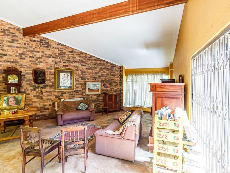 Spacious living room featuring a vaulted ceiling with exposed timber beams and a prominent face-brick feature wall, offering potential for modern renovation.