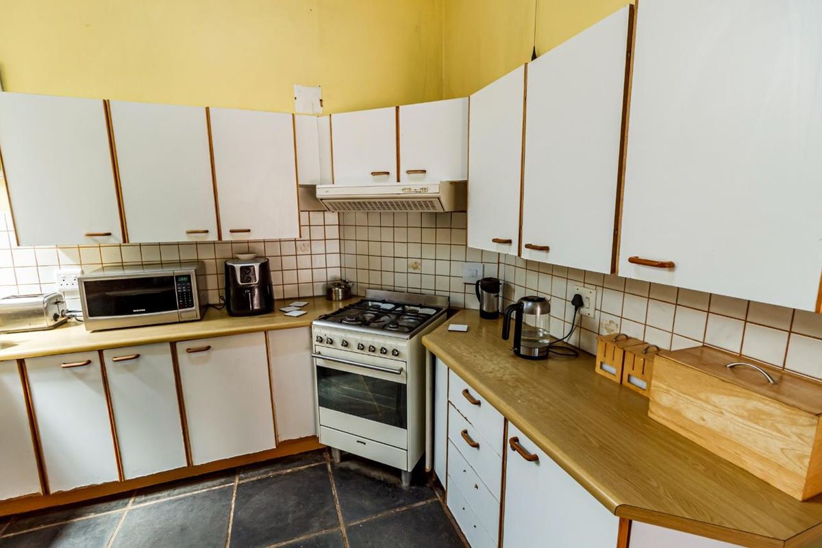 A dated kitchen featuring white cabinetry, gas stove with extractor, tiled backsplash, and dark floor tiles, offering potential for a modern renovation.