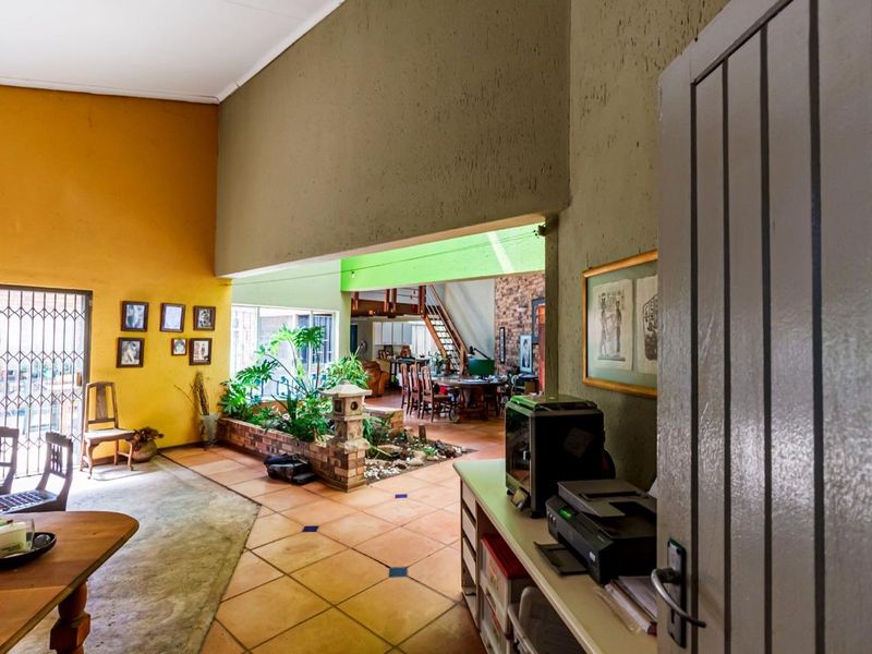 Spacious open-plan living area featuring tiled floors, a unique indoor planter, and an exposed brick feature wall with staircase access.
