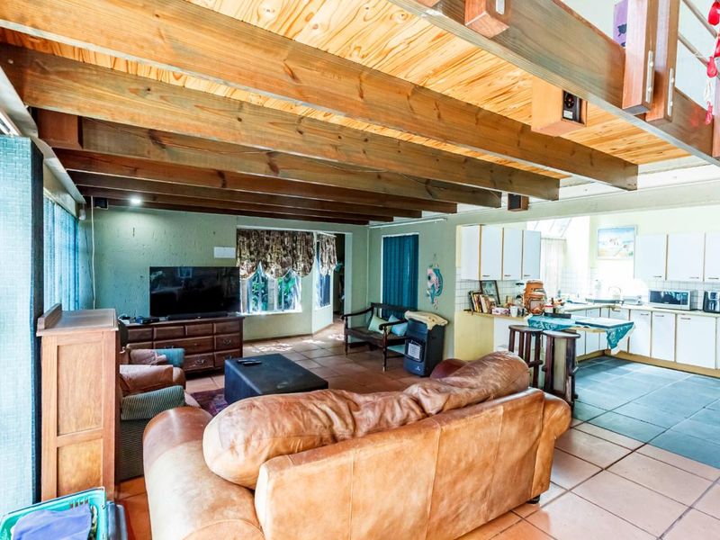 Open-plan living and kitchen area featuring exposed timber ceiling beams, tiled flooring, and a functional kitchen layout with built-in cabinetry.