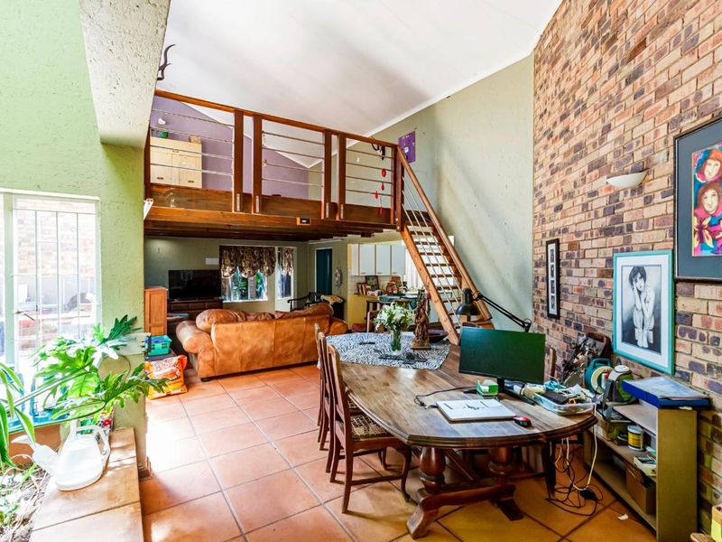 Spacious open-plan living area featuring a double-volume vaulted ceiling, exposed brick feature wall, and a mezzanine level accessible via a wooden staircase.