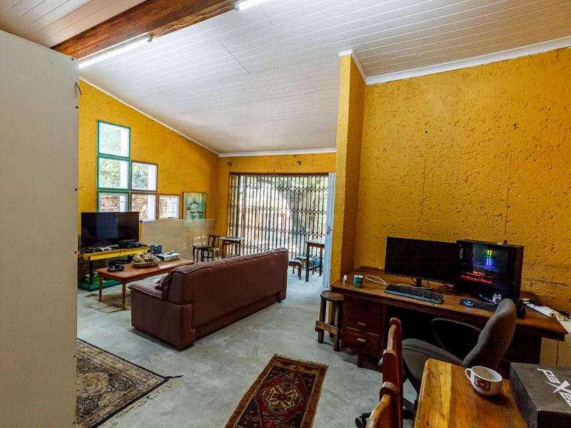 Spacious living area featuring exposed timber ceiling beams, concrete flooring, and large windows with security gates, offering a rustic aesthetic with potential for modernization.