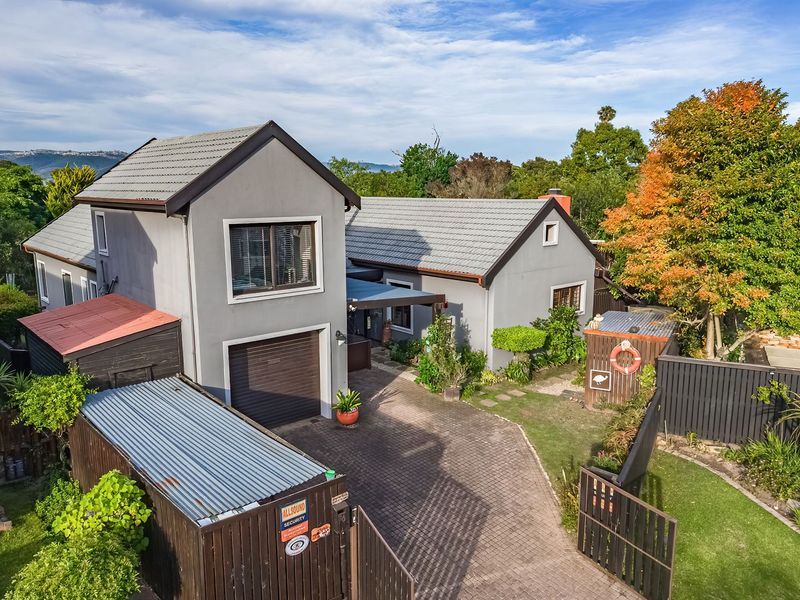 Aerial view of the property featuring a paved driveway, garage, and established garden with mature trees and timber fencing.