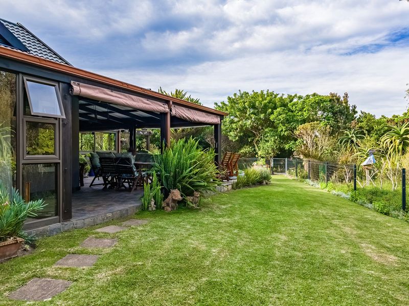 A well-maintained rear garden featuring a spacious covered patio with tiled flooring, overlooking a lush lawn and established greenery.