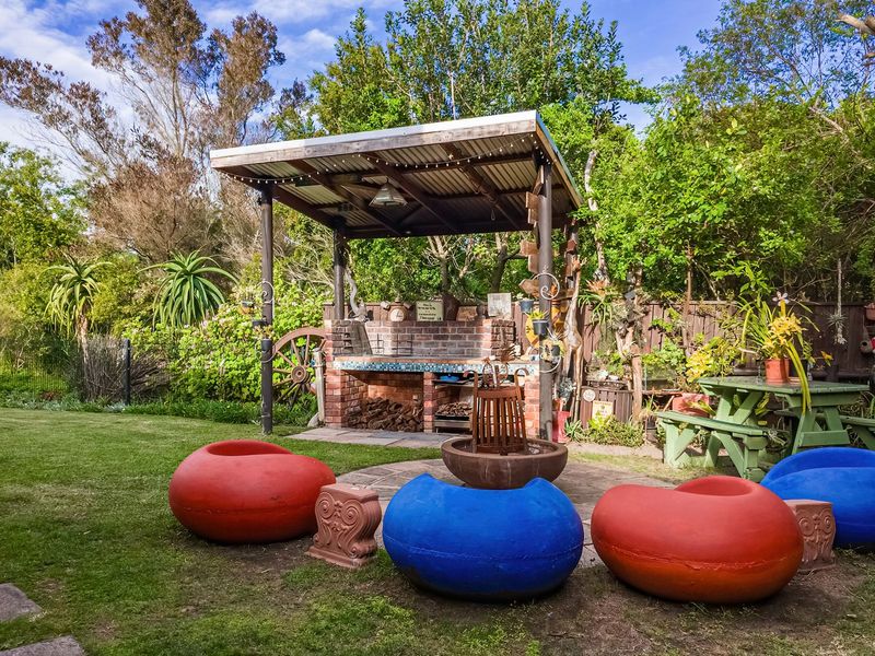 Outdoor entertainment area featuring a covered patio with a built-in brick braai, set within a landscaped garden.
