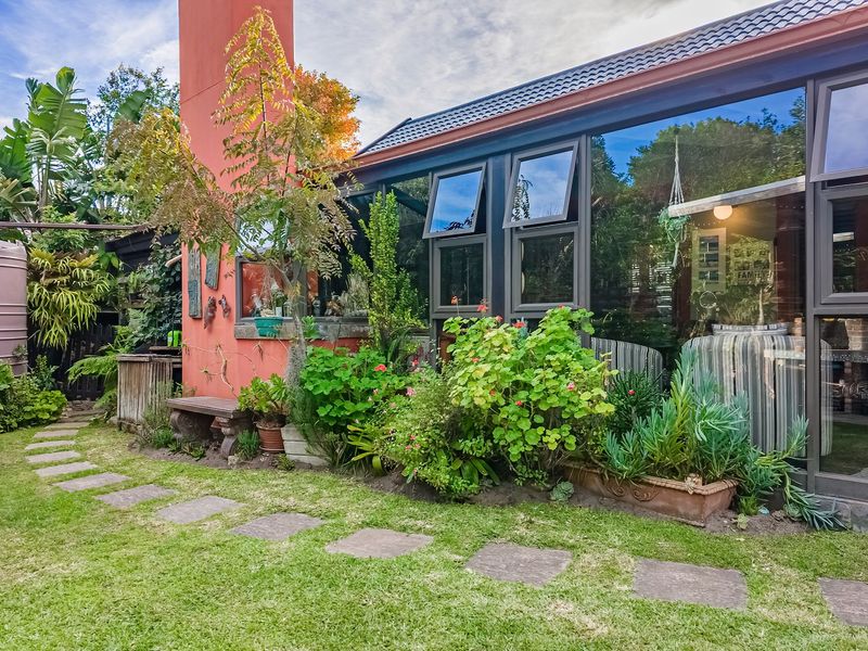 Rear garden view featuring a lawn, stone paver path, water tank, and a prominent chimney against the house exterior with large glass windows.