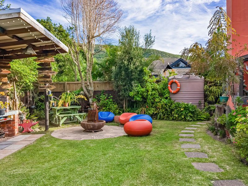 A landscaped rear garden featuring a covered patio with a built-in brick braai, stone pathways, and a water tank.