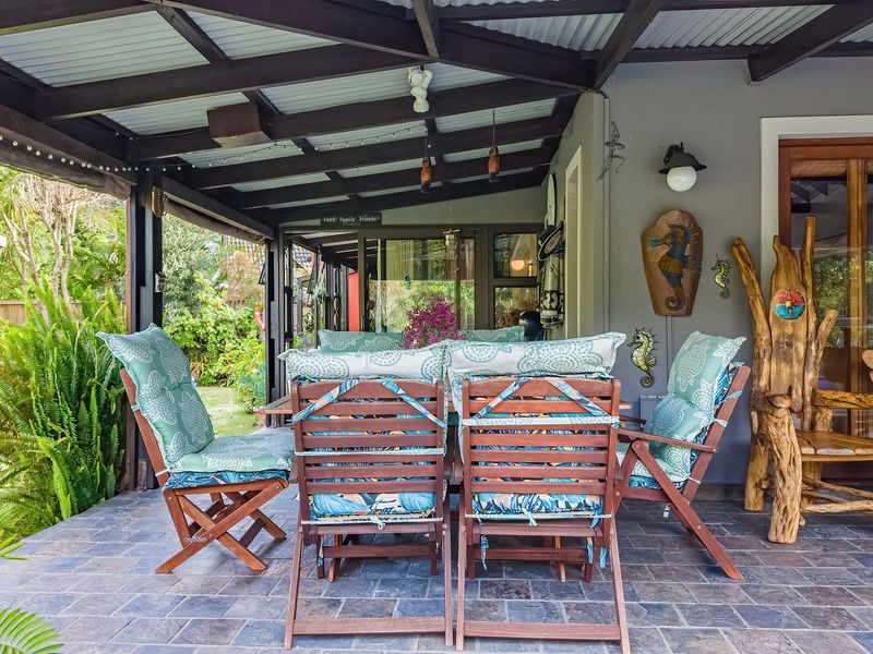 A covered outdoor patio featuring slate tile flooring and exposed timber rafters, providing a seamless transition to the garden area through sliding glass doors.