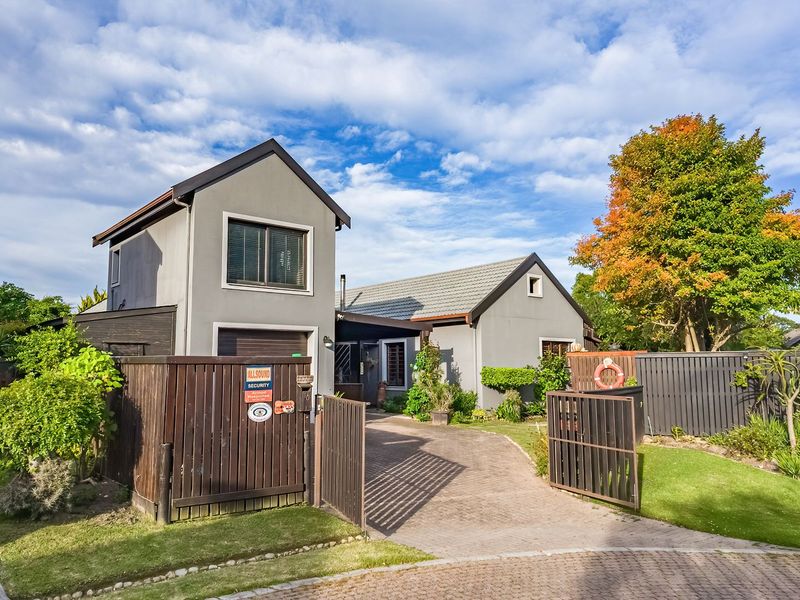 Front exterior view of a residential property featuring a paved driveway, secure gated entrance, and well-maintained garden area.