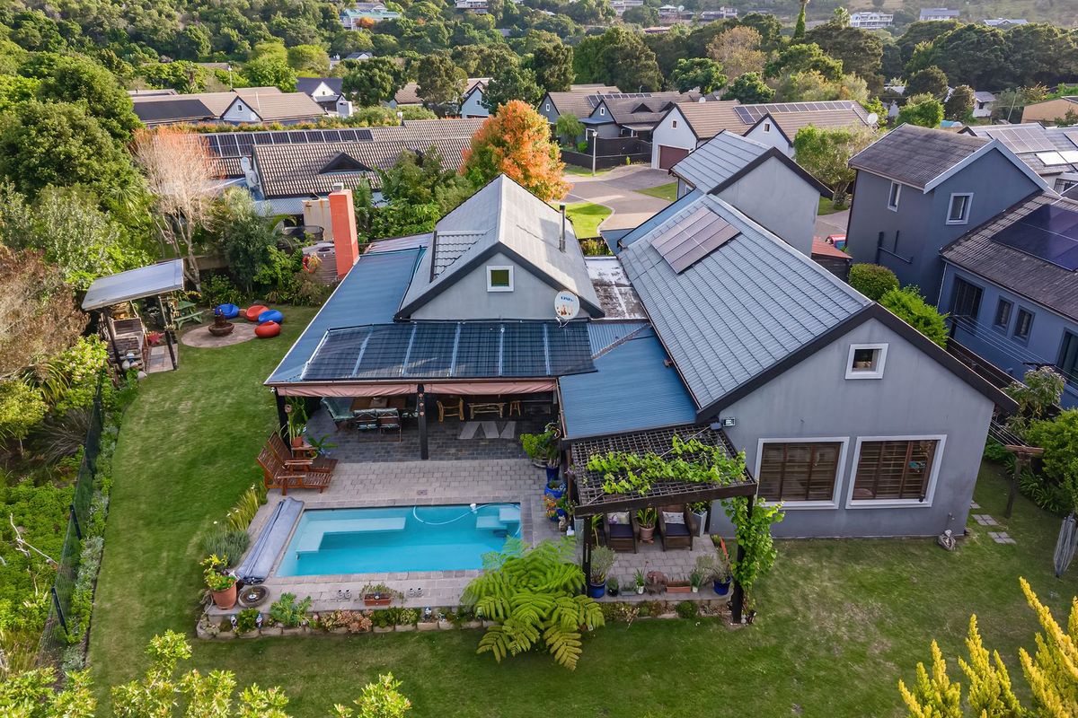 Aerial view of a residential property featuring a swimming pool, paved patio area, pergola, and solar panels installed on the tiled roof.