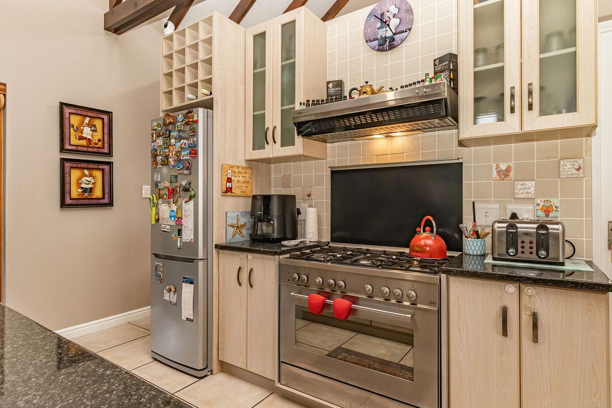 A functional kitchen featuring light wood cabinetry, granite countertops, a gas stove with extractor fan, and exposed timber ceiling beams.