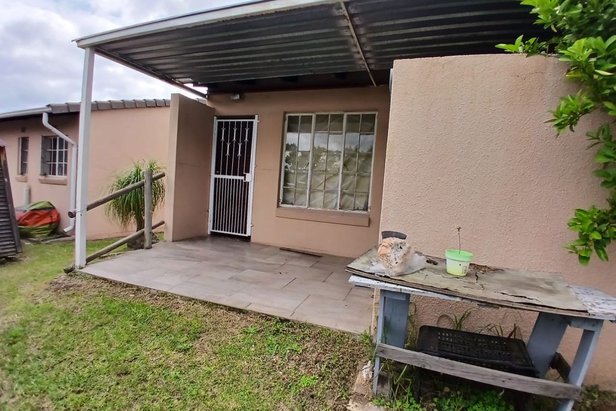 A covered patio area featuring tiled flooring, a corrugated metal roof, and a security gate, providing a functional outdoor space for the townhouse.