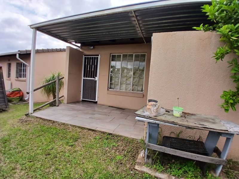 A covered patio area featuring tiled flooring, a corrugated metal roof, and a security gate, providing a functional outdoor space for the townhouse.