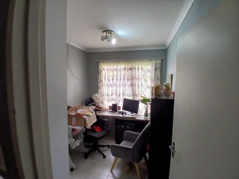 A compact home office featuring tiled flooring, coving, and a built-in desk area, currently used as a workspace.