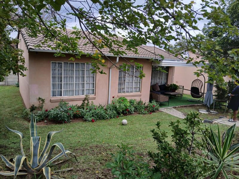 Rear view of the townhouse featuring a tiled roof, a paved patio area, and a well-maintained garden with established landscaping.