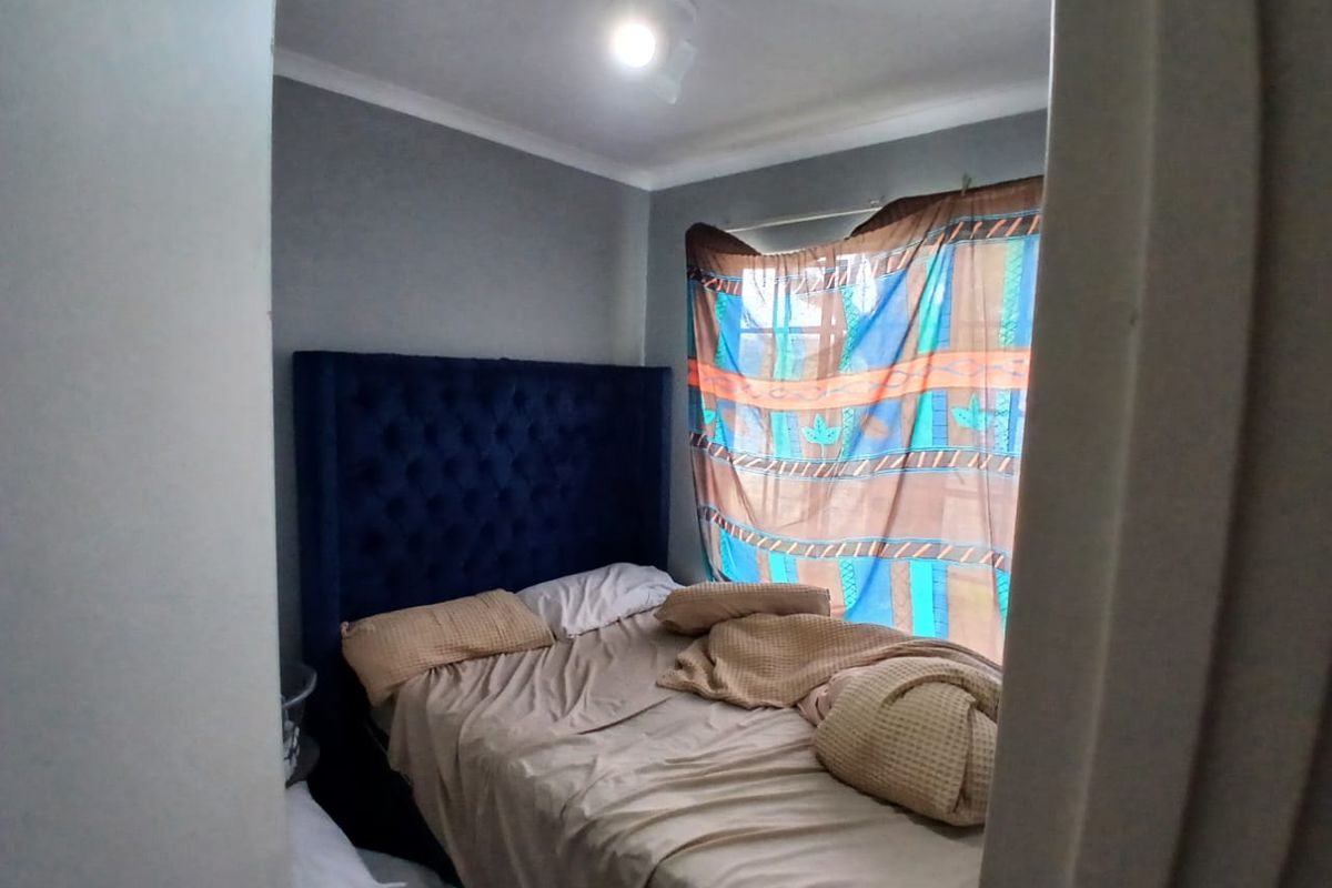 A compact bedroom featuring grey walls, a ceiling light fixture, and a window with curtains.