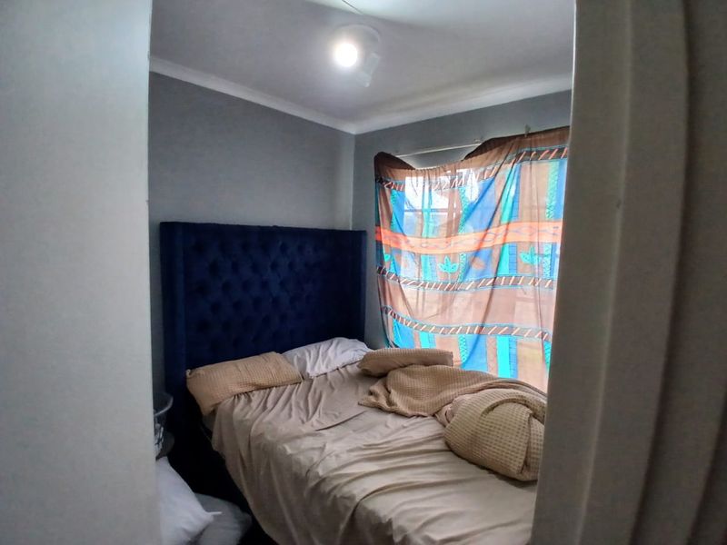 A compact bedroom featuring grey walls, a ceiling light fixture, and a window with curtains.
