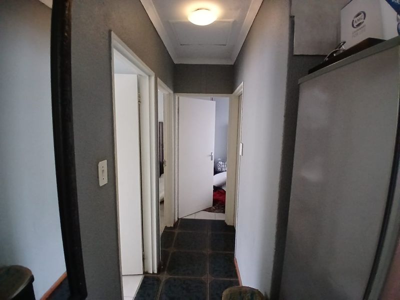 A narrow residential hallway featuring tiled flooring and access to multiple rooms, showing signs of wear and requiring cosmetic updates.