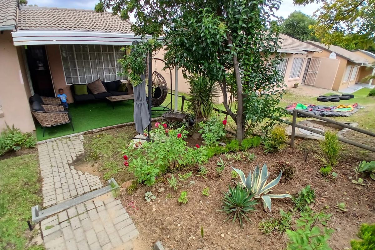 A rear view of the townhouse featuring a covered patio area, a paved walkway, and a landscaped garden with established trees and shrubs.