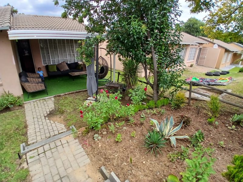A rear view of the townhouse featuring a covered patio area, a paved walkway, and a landscaped garden with established trees and shrubs.