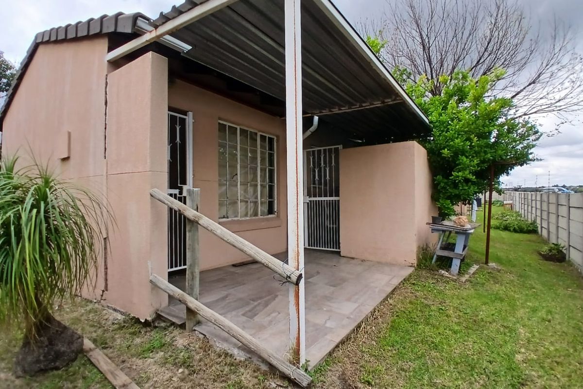 A covered rear patio area featuring tiled flooring, a corrugated metal roof, and security gates, showing signs of wear and structural weathering.