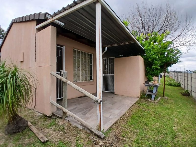 A covered rear patio area featuring tiled flooring, a corrugated metal roof, and security gates, showing signs of wear and structural weathering.
