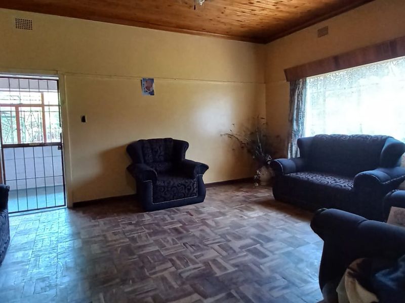 A spacious living room featuring classic parquet flooring and a warm timber ceiling, offering a traditional aesthetic with ample natural light.