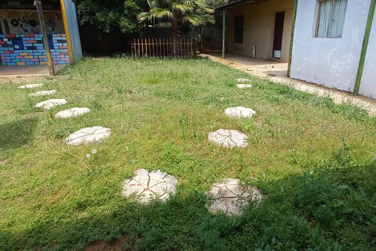 Rear garden area featuring a stepped stone path, overgrown lawn, and access to a covered patio and adjacent building structures.