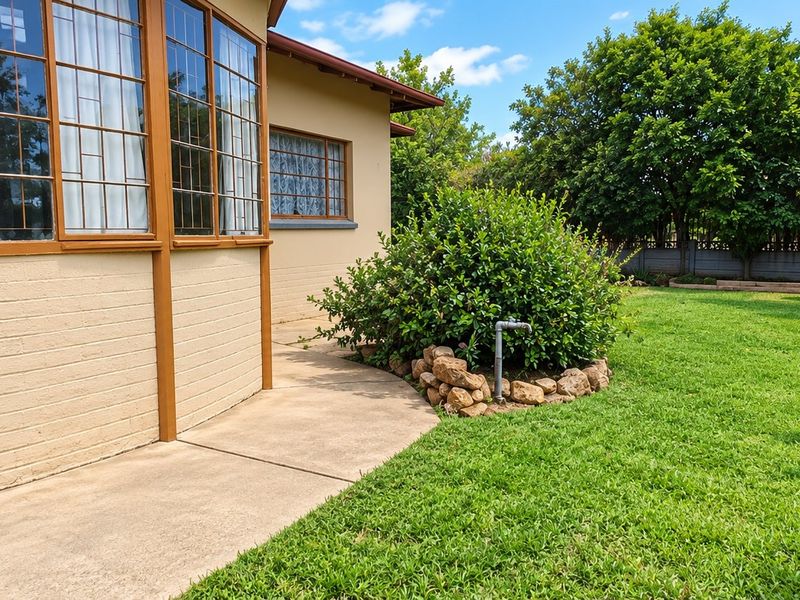A well-maintained rear garden featuring a concrete pathway, established lawn, and a brick exterior wall with leaded glass windows.