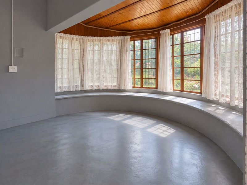 Bright living area featuring a unique curved built-in window seat, polished concrete floors, and a warm timber-paneled ceiling with large leaded glass windows.