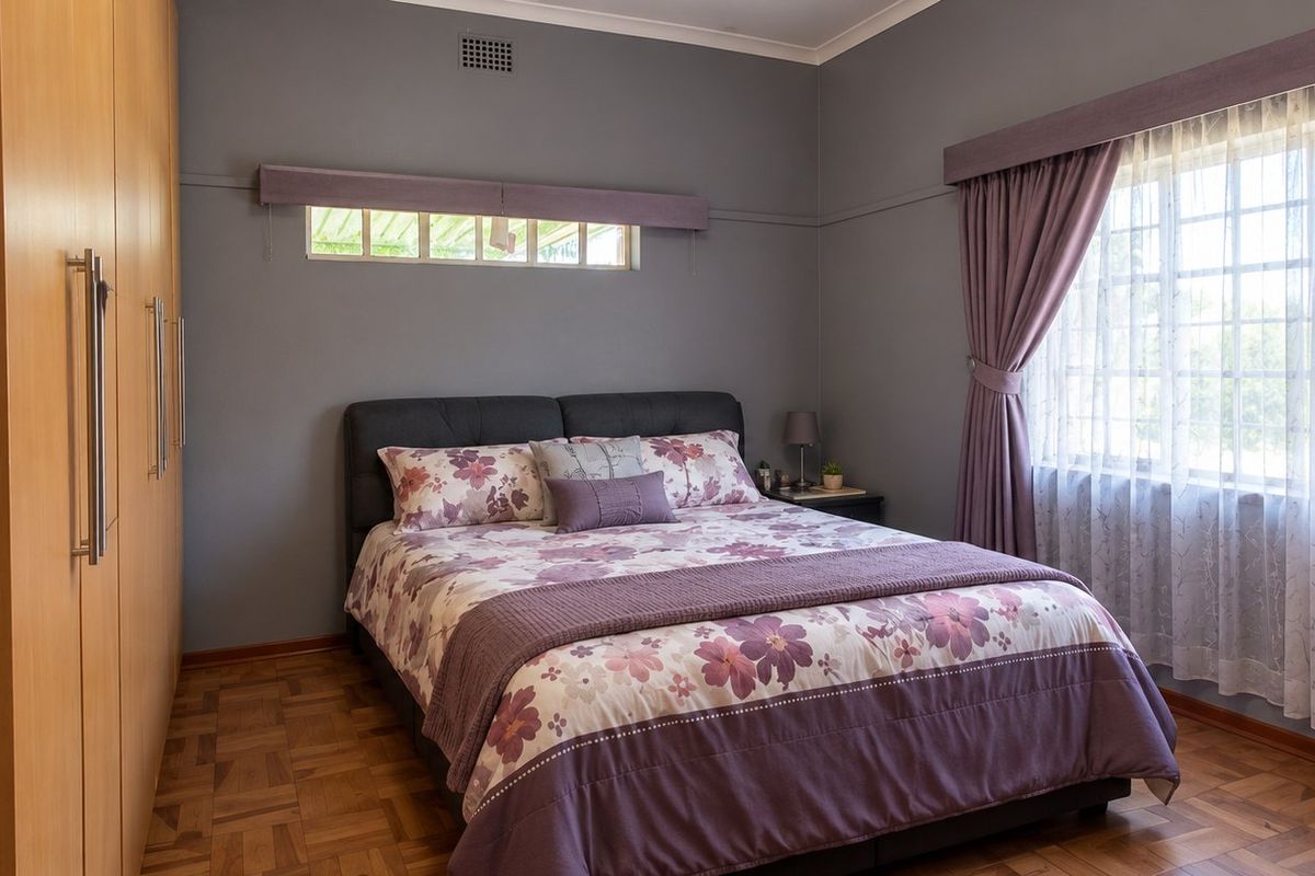 A well-maintained bedroom featuring classic parquet flooring, ample built-in cupboard storage, and large windows with security bars.