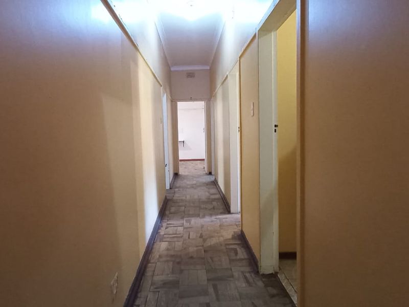 A long, empty residential hallway featuring parquet flooring and coved ceilings, providing access to multiple rooms throughout the property.