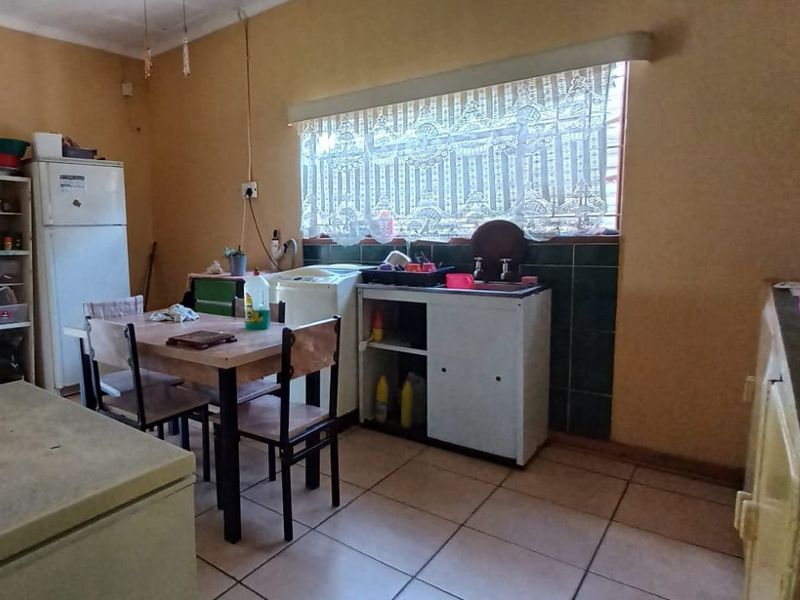 A functional kitchen space featuring tiled flooring, a built-in sink area with tiled splashback, and ample natural light from a large window.