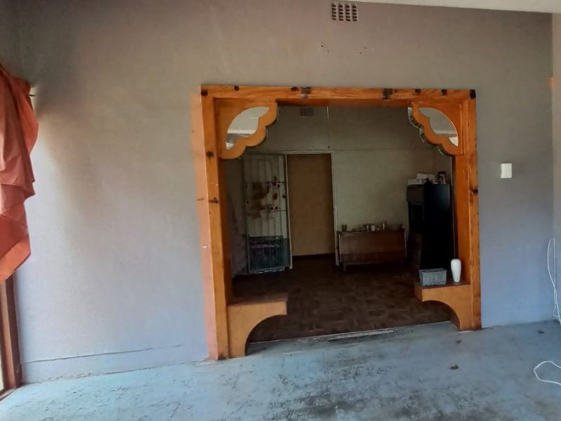 Living area featuring a distinctive decorative timber archway, sliding glass door access, and dated finishes requiring modernization.