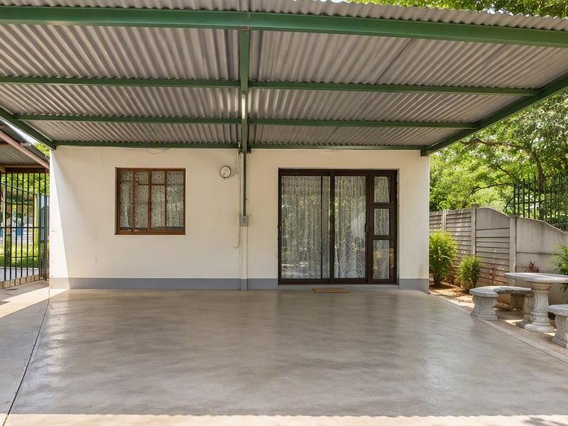 A covered outdoor patio area featuring a corrugated metal roof, concrete flooring, and direct access to the interior through a sliding glass door.