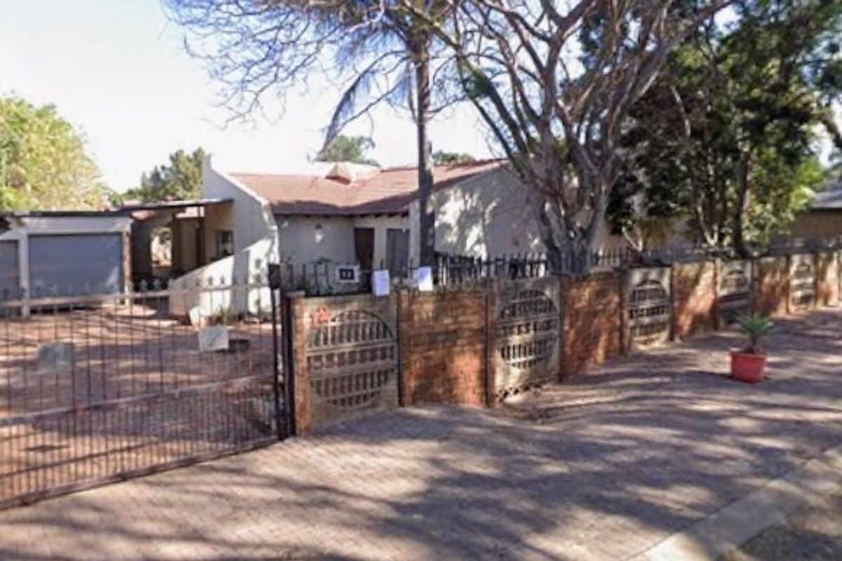 Front exterior view of a townhouse featuring a brick boundary wall, metal driveway gate, and paved access to the garage.
