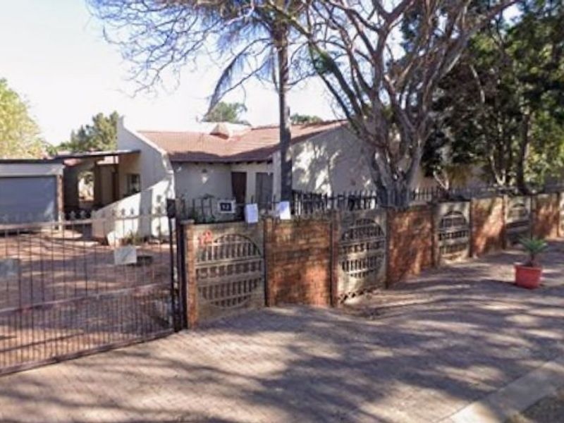 Front exterior view of a townhouse featuring a brick boundary wall, metal driveway gate, and paved access to the garage.