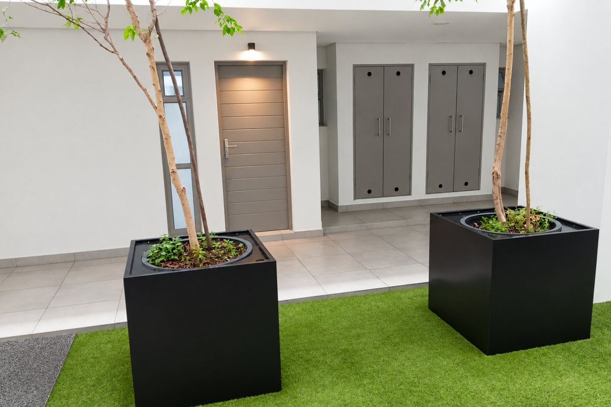 A modern, well-maintained rear courtyard featuring tiled flooring, artificial grass, and integrated storage cupboards with a secure external access door.