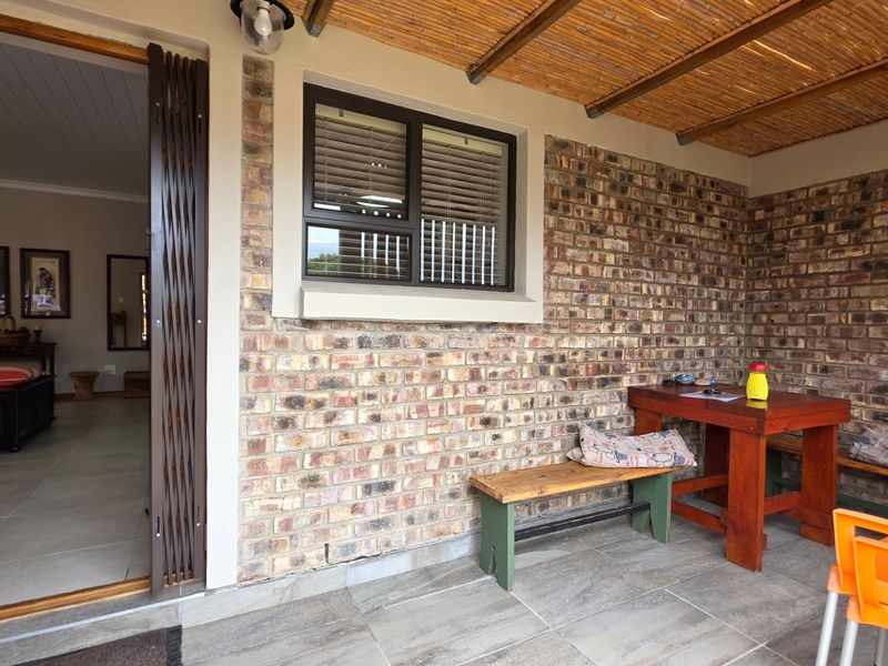 A covered patio area featuring exposed brick walls, tiled flooring, and a bamboo roof structure, providing a comfortable outdoor living space.