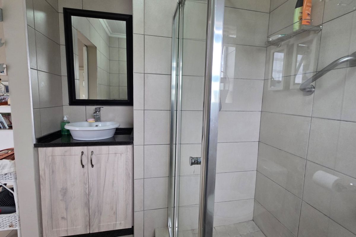 A functional bathroom featuring a modern vessel sink on a vanity cabinet, a framed mirror, and a glass-enclosed shower with tiled walls.