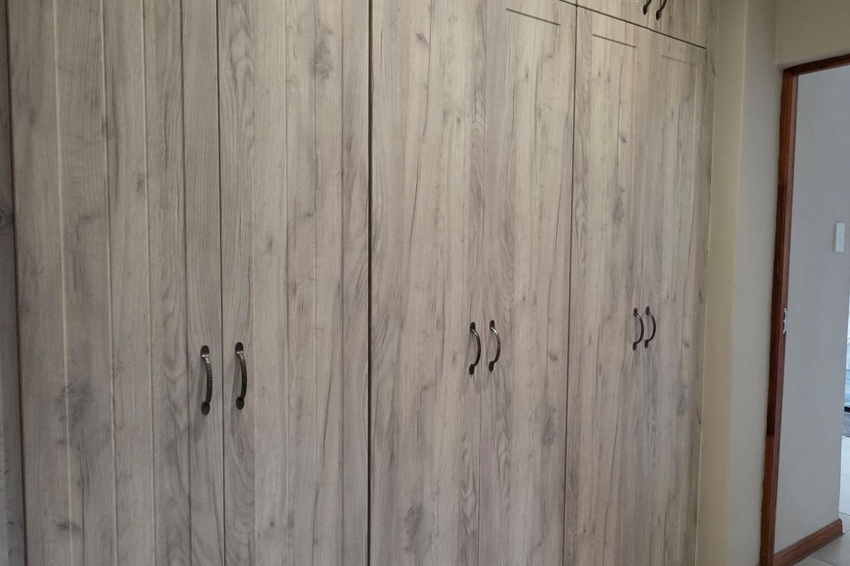 A bedroom featuring extensive built-in cupboards with a light wood-grain finish and neutral tiled flooring.