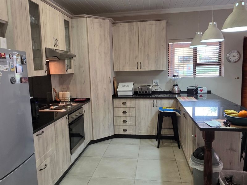 A functional kitchen featuring light wood-grain cabinetry, dark granite countertops, a breakfast bar, and integrated appliances, complemented by tiled flooring and modern pendant lighting.