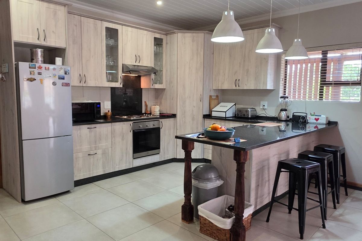 Modern kitchen featuring light wood-grain cabinetry, granite countertops, a central island with breakfast bar seating, and integrated appliances.
