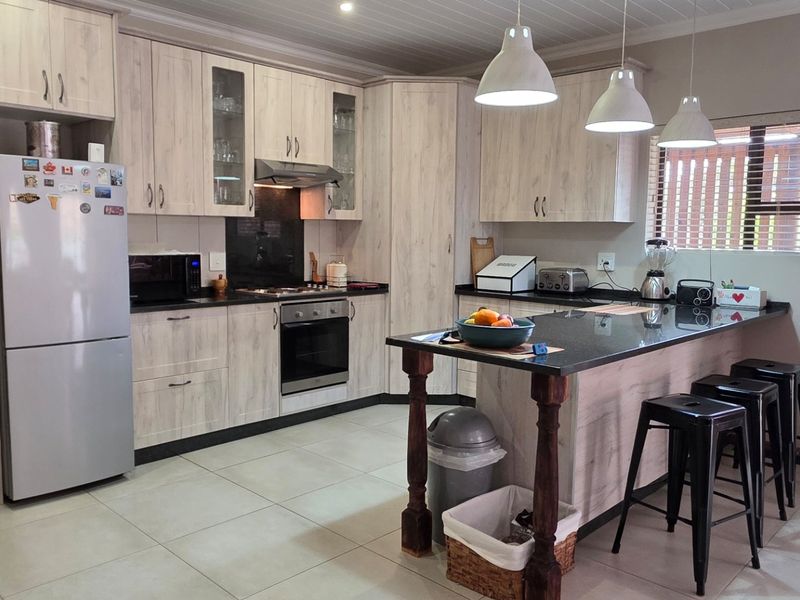 Modern kitchen featuring light wood-grain cabinetry, granite countertops, a central island with breakfast bar seating, and integrated appliances.