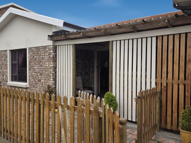 A covered patio area featuring a timber pergola and privacy screening, complemented by a brick facade and a paved outdoor space with picket fencing.