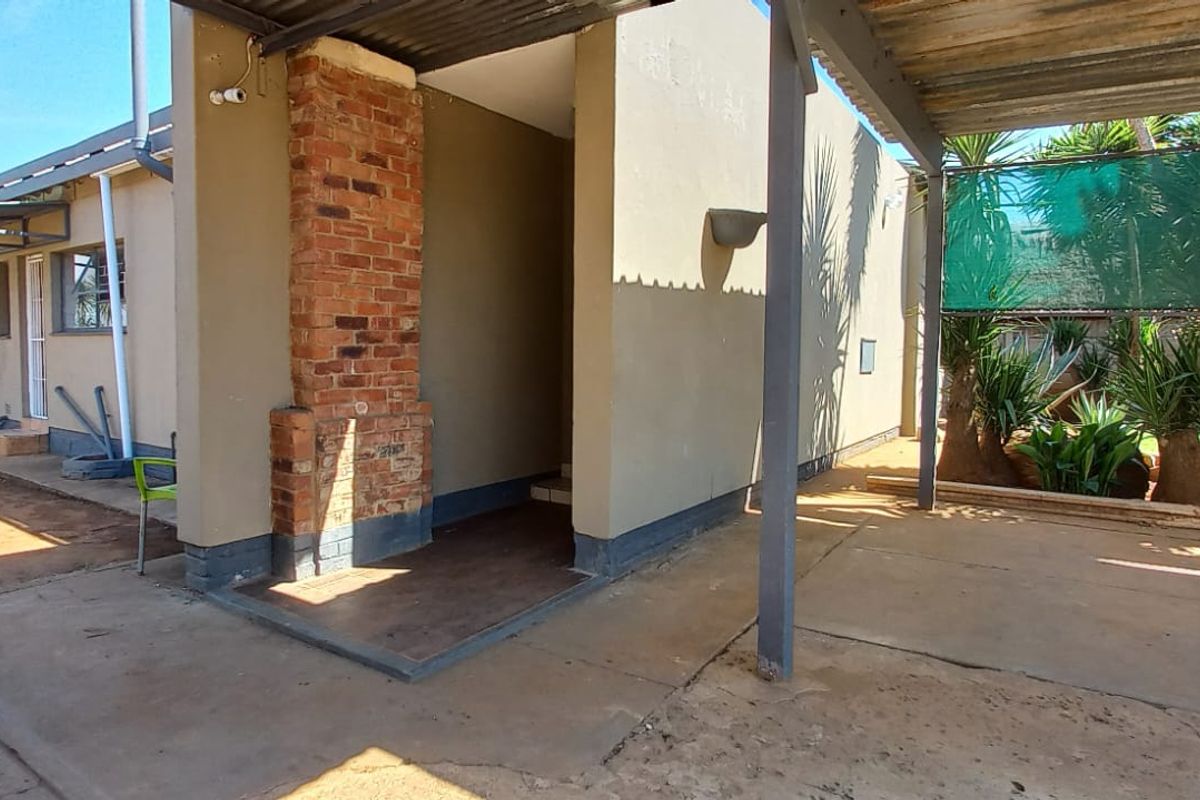 Rear exterior view featuring a covered patio area with a brick chimney, concrete flooring, and shade cloth screening.