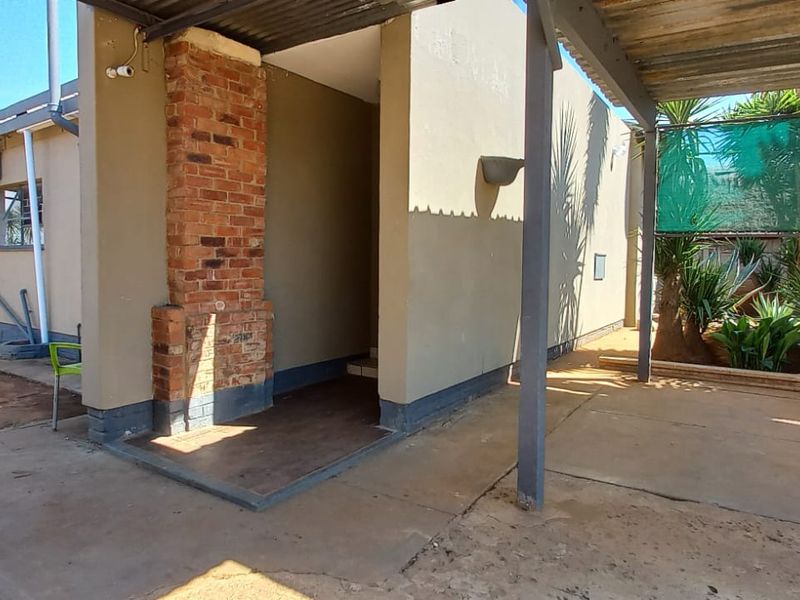 Rear exterior view featuring a covered patio area with a brick chimney, concrete flooring, and shade cloth screening.