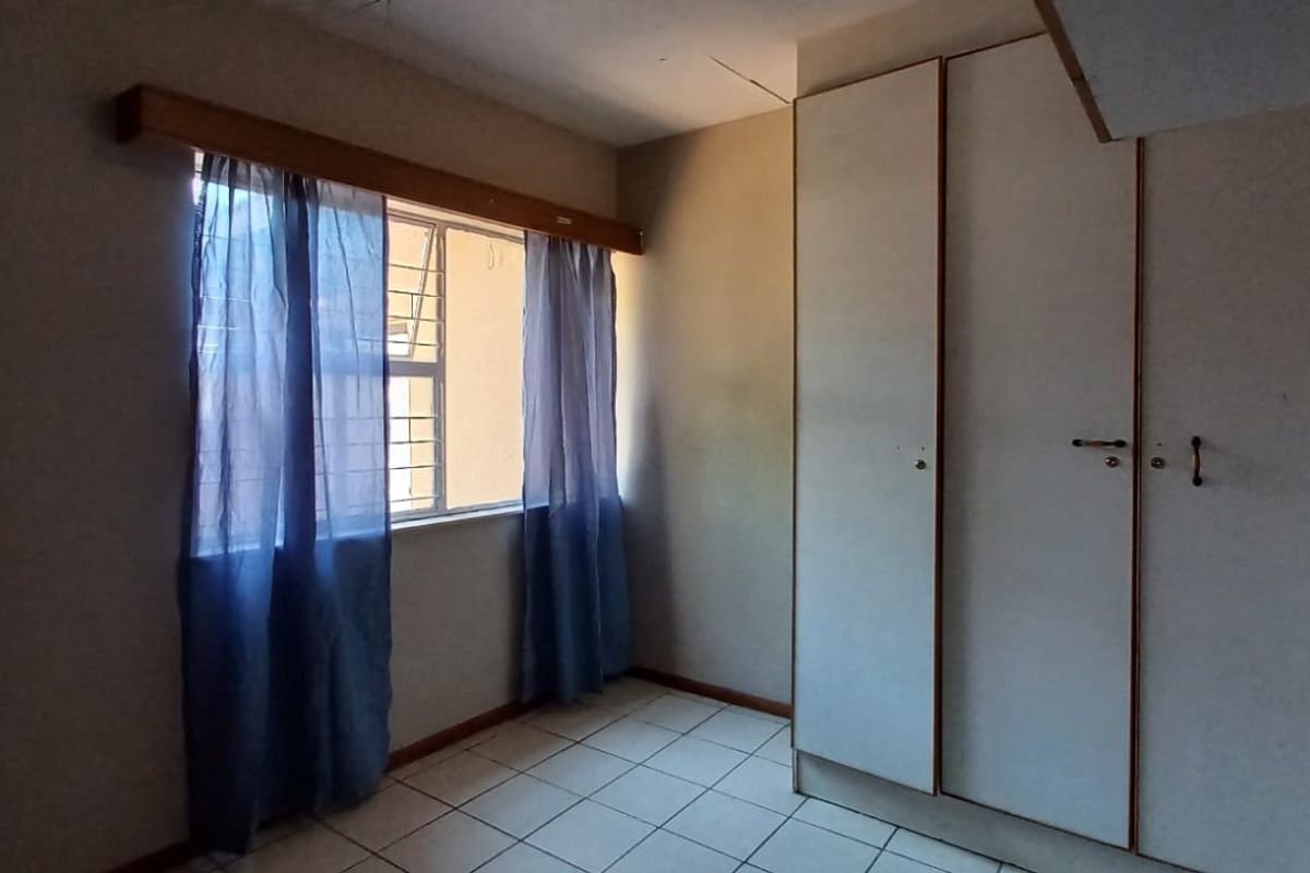 A vacant bedroom featuring tiled flooring, built-in cupboards, and window security bars, requiring minor cosmetic updates to the ceiling and cabinetry.