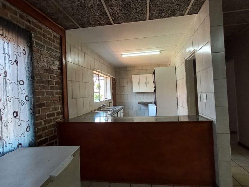 A dated kitchen featuring exposed brick walls, tiled backsplash, and a breakfast counter, offering potential for a modern renovation.