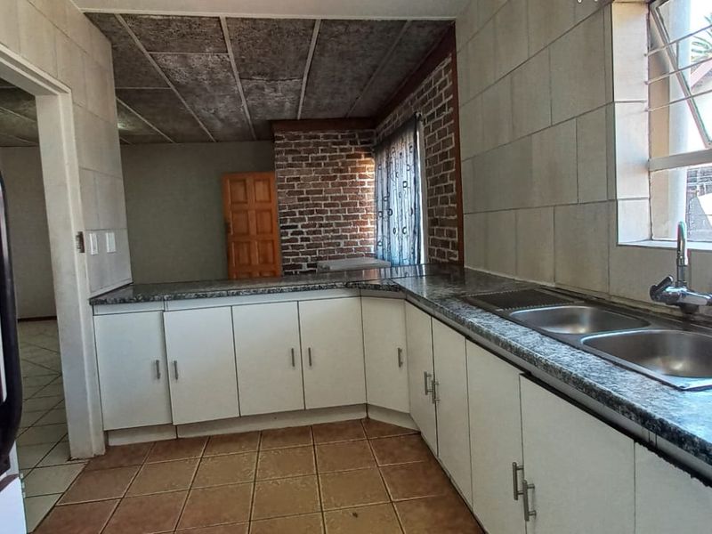 A functional kitchen featuring laminate countertops, a double basin sink, tiled flooring, and an exposed brick feature wall, offering potential for modern renovation.